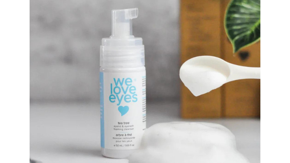 "We Love Eyes Foaming cleanser sitting on a countertop with a spoon scooping up foam sitting on the counter"