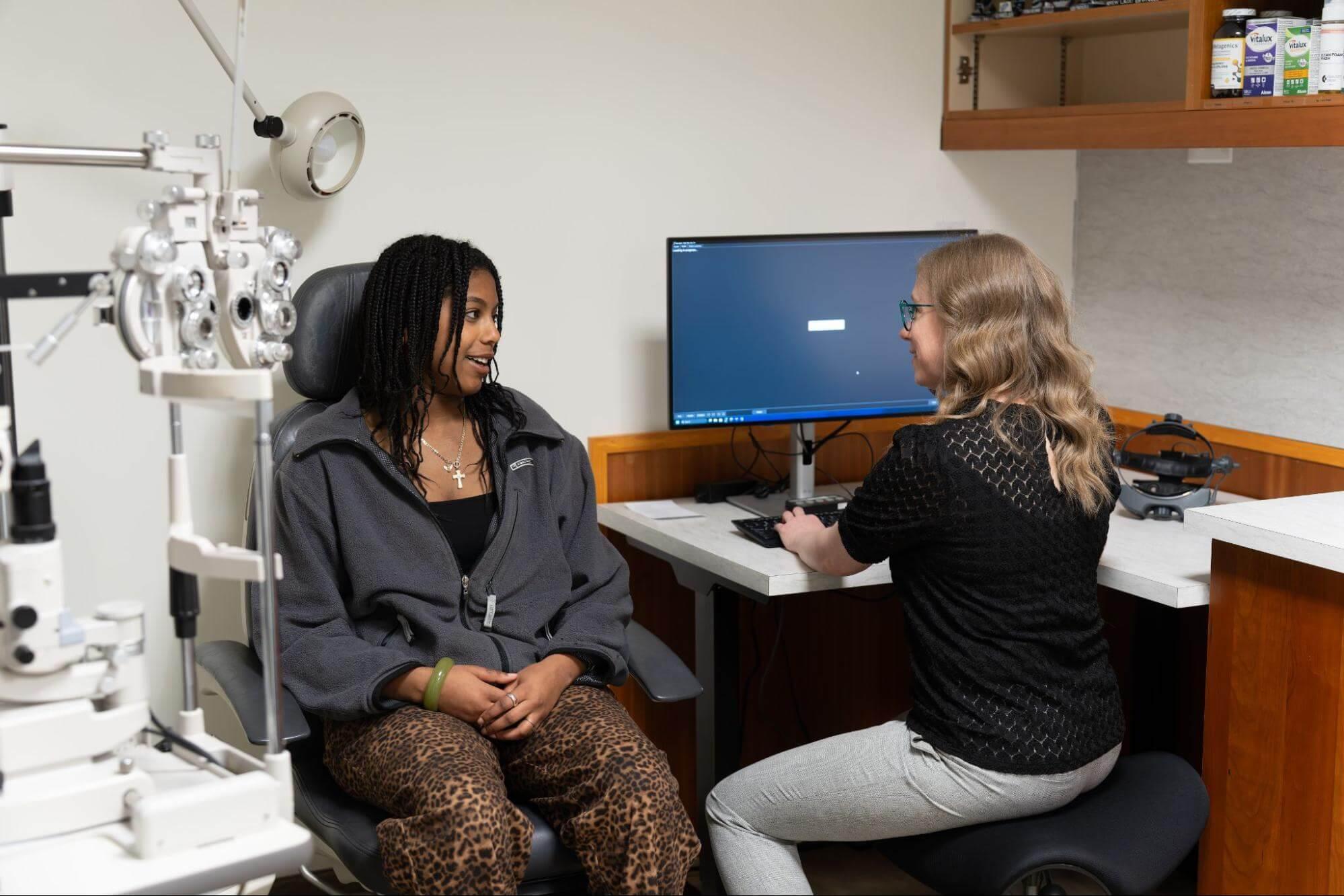 Optometrist discussing eye exam results with a patient while reviewing information on a computer in an exam room.